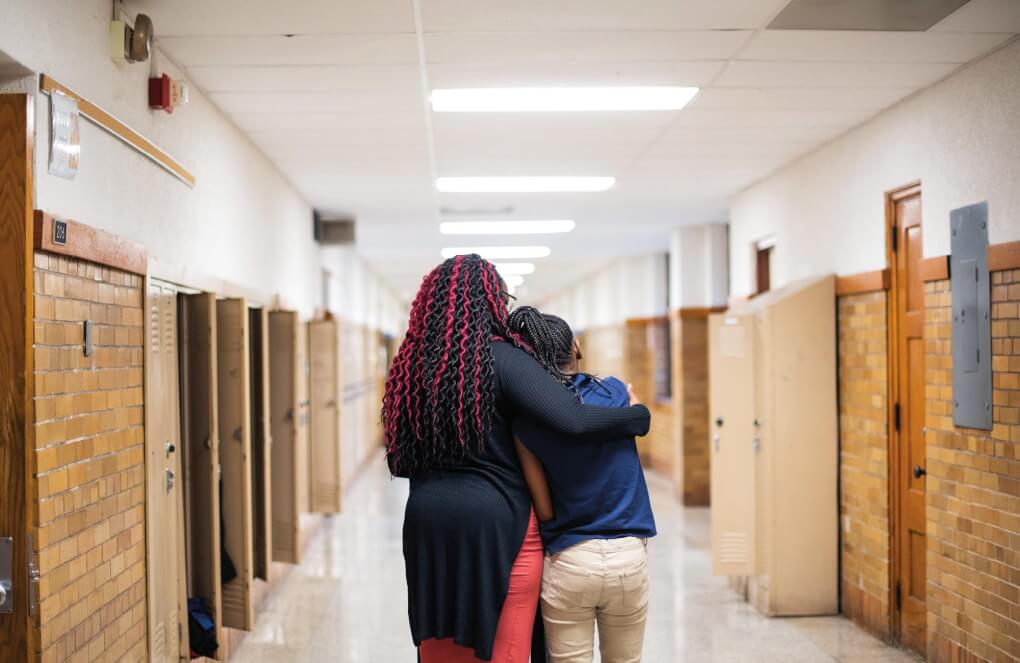 A teacher and student walk down a hall together